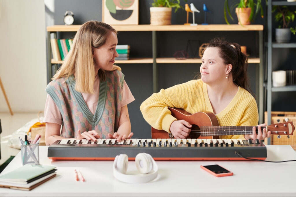 Young woman with Down syndrome and her music therapist at home playing synth and guitar